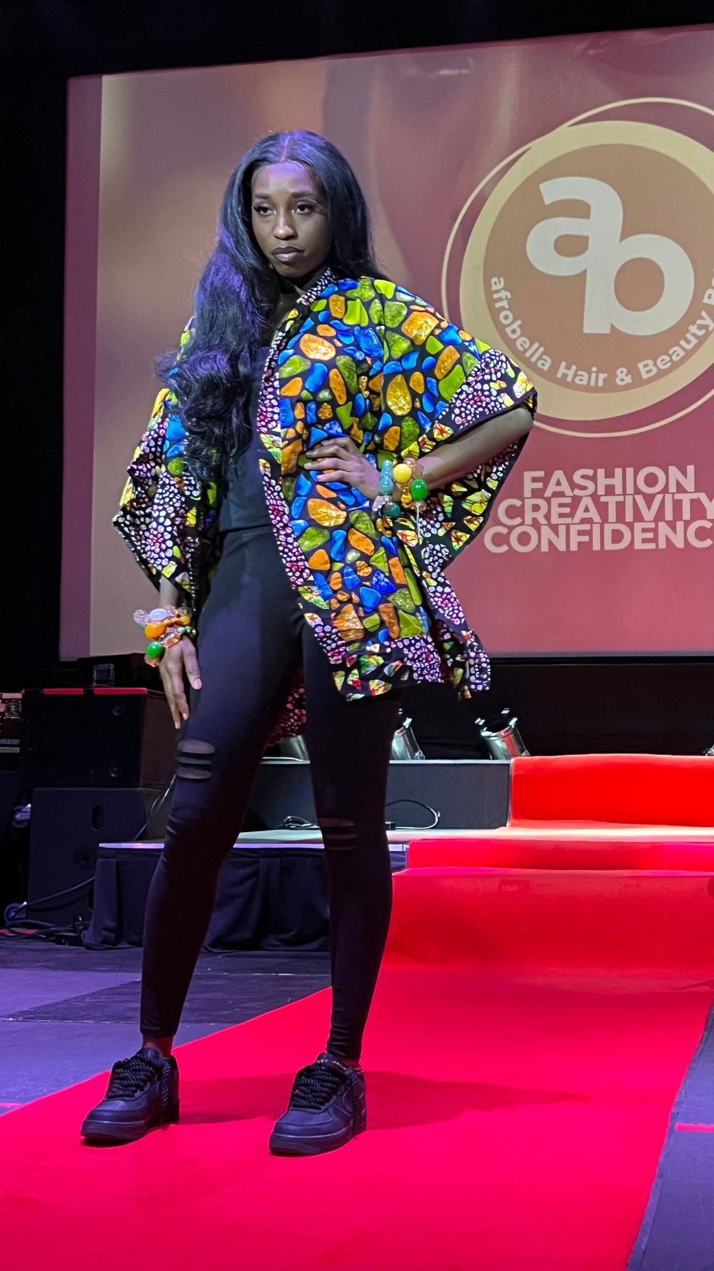 Model on a catwalk wearing a colorful outfit with 'AB' logo in the background